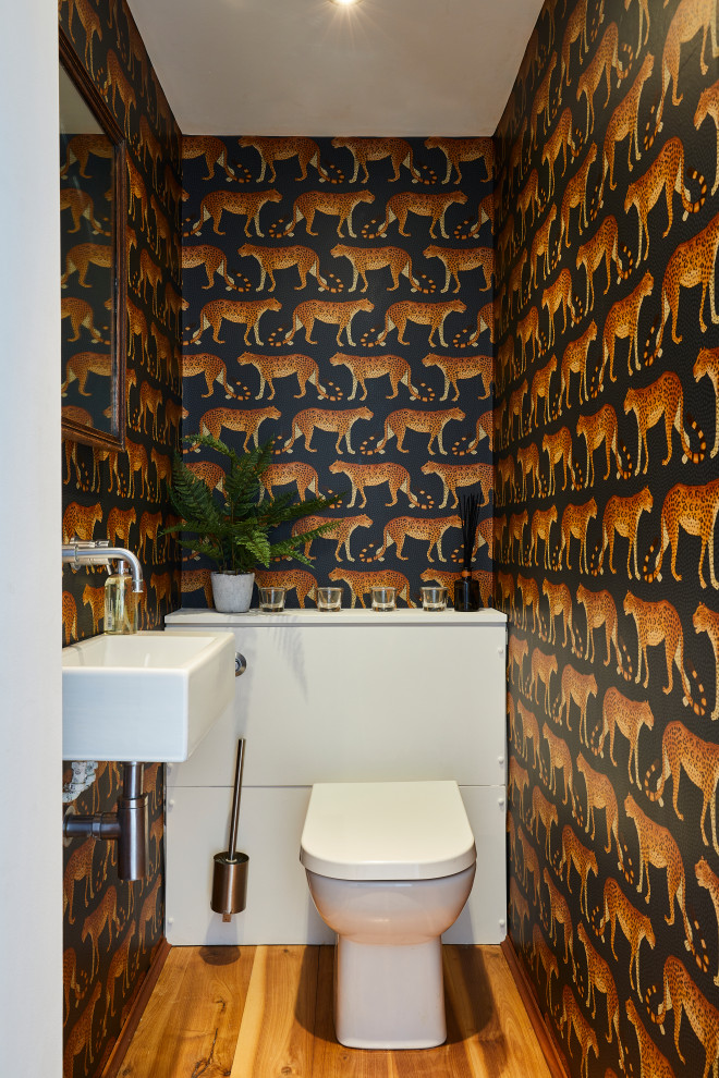 Cette image montre un WC et toilettes design avec un mur multicolore, un sol en bois brun, un lavabo suspendu et un sol marron.