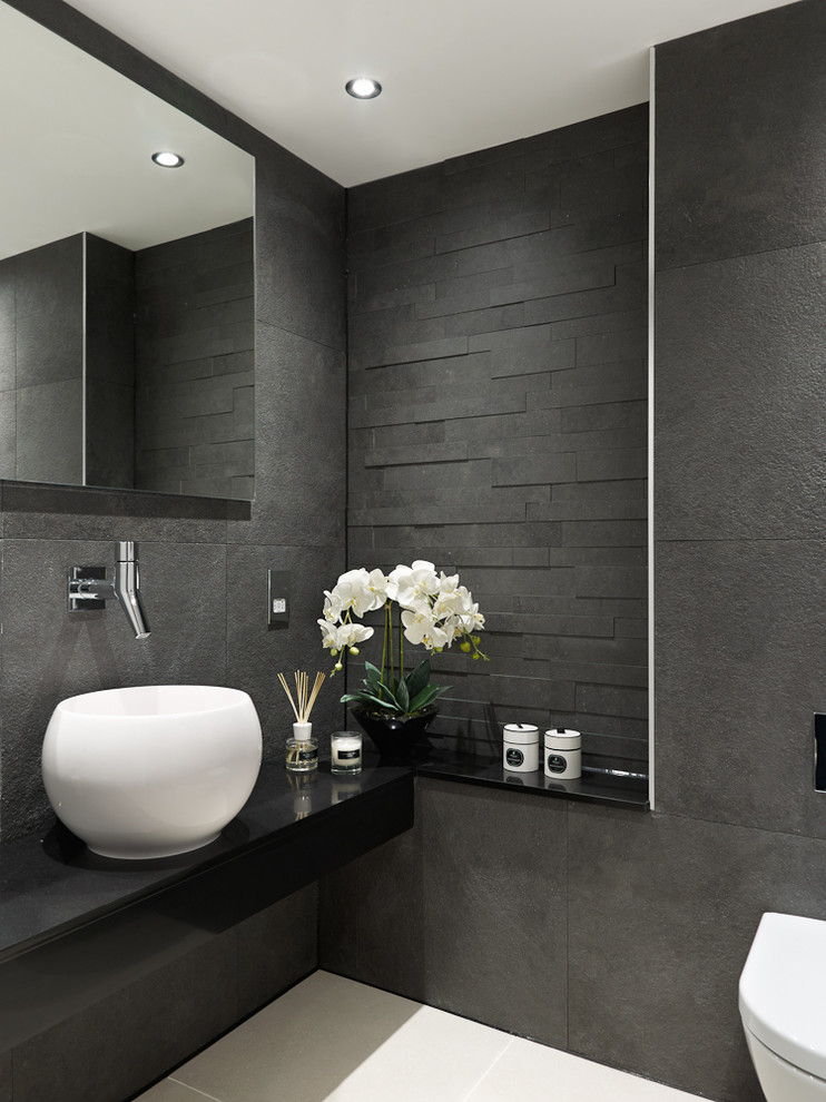 Inspiration for a contemporary cloakroom in Surrey with a vessel sink, a wall mounted toilet, grey tiles, black tiles, grey walls and black worktops.