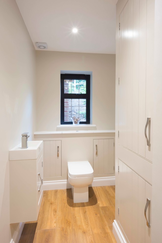 Idée de décoration pour un grand WC suspendu champêtre avec un placard à porte shaker, des portes de placard blanches, un mur blanc, un sol en bois brun, un plan vasque, un plan de toilette en bois et un sol marron.
