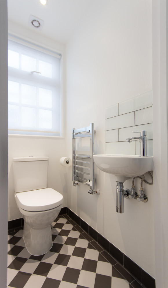 Cette image montre un petit WC et toilettes design avec WC à poser, un carrelage noir et blanc, un mur blanc, un sol en carrelage de porcelaine, un lavabo suspendu et des plaques de verre.