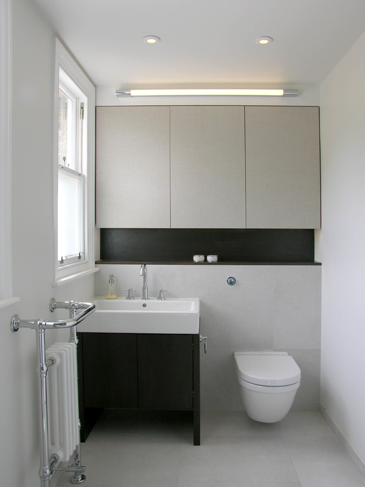 Imagen de aseo actual con lavabo integrado, armarios con paneles lisos, sanitario de pared, baldosas y/o azulejos grises y paredes blancas