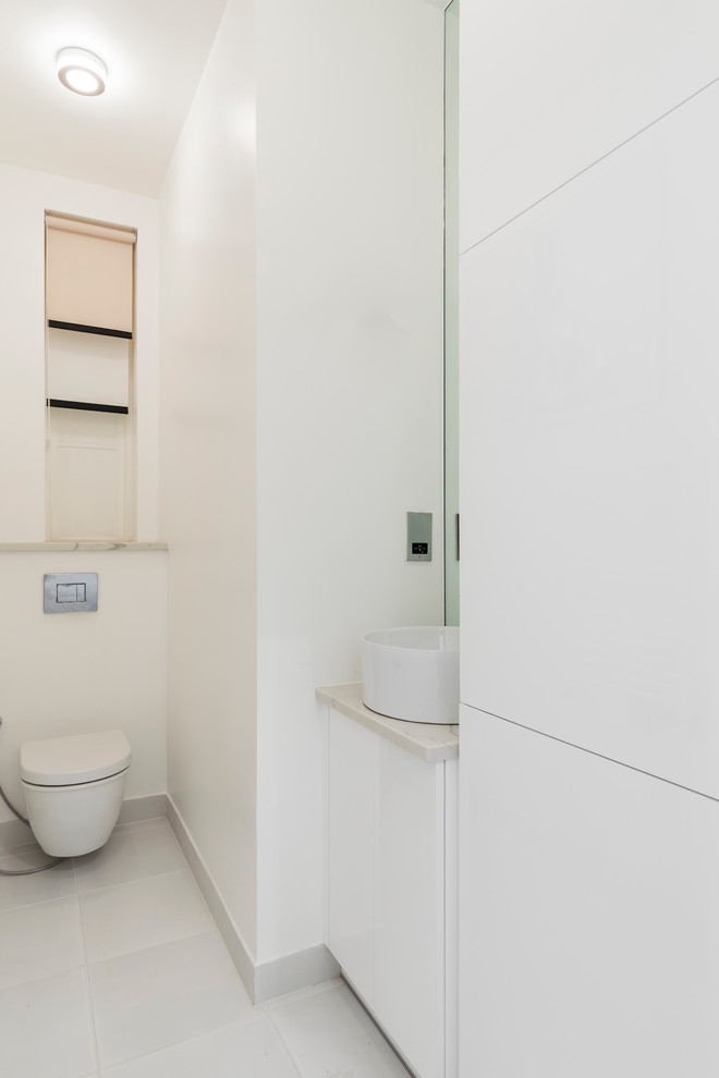 Idée de décoration pour un petit WC suspendu design avec un placard à porte plane, des portes de placard blanches, un carrelage blanc, un mur blanc, un sol en carrelage de porcelaine, une vasque, un plan de toilette en marbre, un sol gris et un plan de toilette gris.