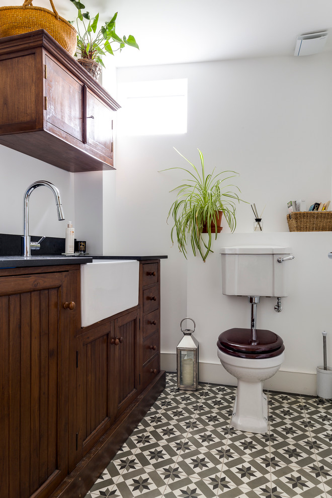 Cette image montre un WC et toilettes traditionnel en bois foncé avec un placard en trompe-l'oeil, un mur blanc, WC séparés et un sol multicolore.