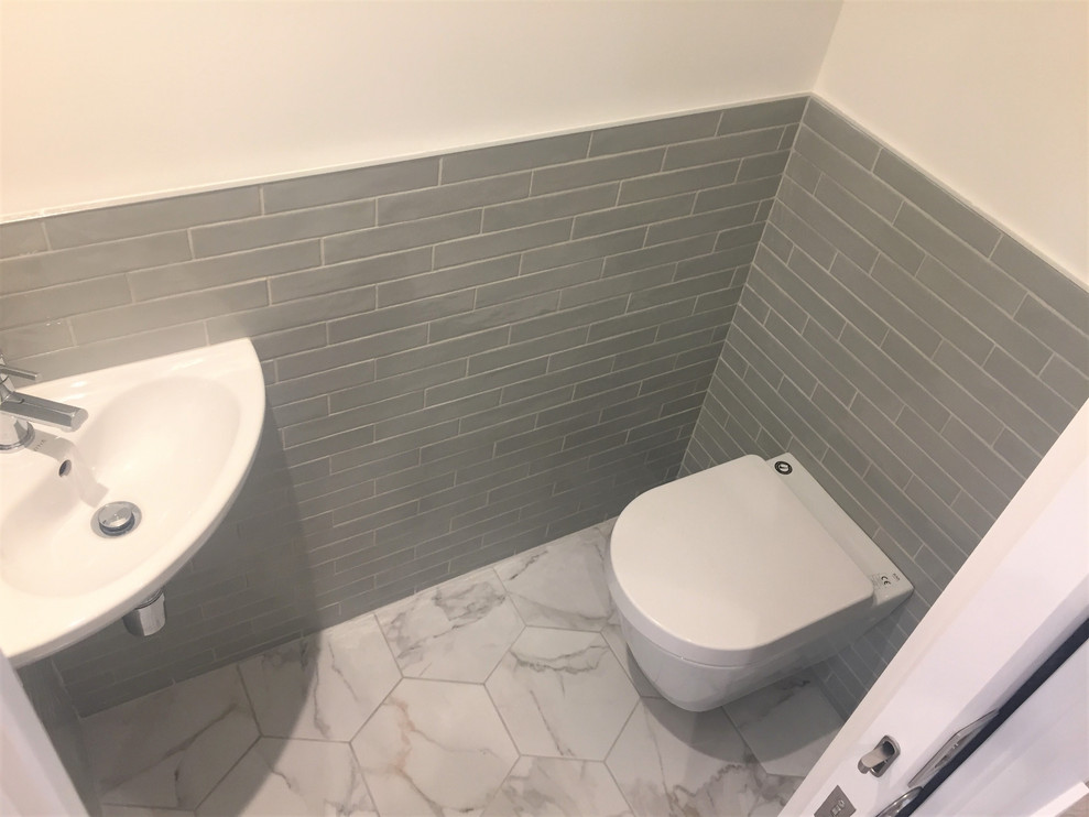 Cette image montre un petit WC et toilettes design avec un carrelage vert, un carrelage métro, un mur blanc, un sol en carrelage de céramique, un lavabo suspendu et un sol gris.