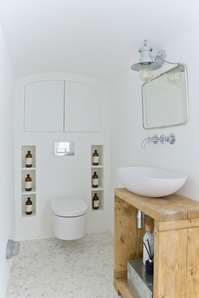 This is an example of a small scandi cloakroom in London with open cabinets, white cabinets, a wall mounted toilet, white walls, mosaic tile flooring, a vessel sink, multi-coloured floors and wooden worktops.