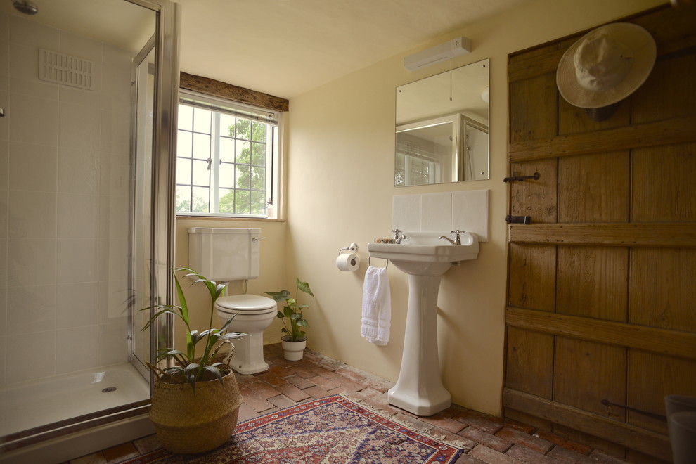 Пример оригинального дизайна: маленький туалет в стиле кантри с раздельным унитазом, белыми стенами, кирпичным полом и раковиной с пьедесталом для на участке и в саду