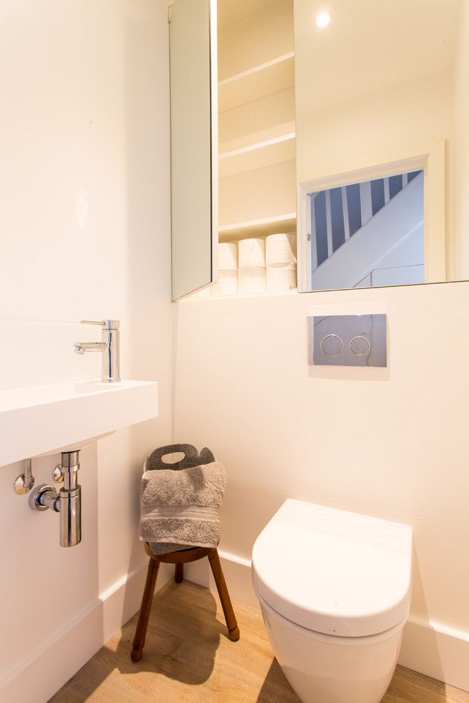 This is an example of a small contemporary cloakroom in Other with a one-piece toilet, white tiles, ceramic tiles, white walls, light hardwood flooring and a wall-mounted sink.