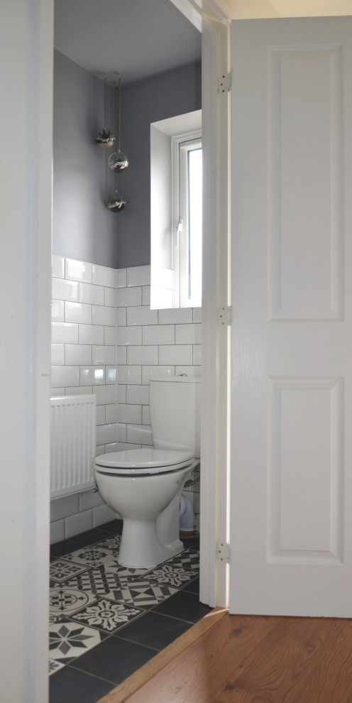Inredning av ett minimalistiskt litet toalett, med en toalettstol med hel cisternkåpa, vit kakel, keramikplattor, grå väggar, klinkergolv i keramik och flerfärgat golv