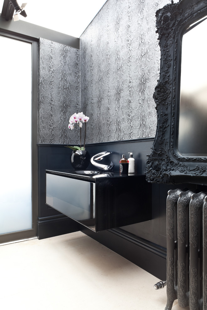 Immagine di un bagno di servizio boho chic di medie dimensioni con lavabo integrato, ante lisce, ante nere, top in vetro, pareti grigie e pavimento in pietra calcarea
