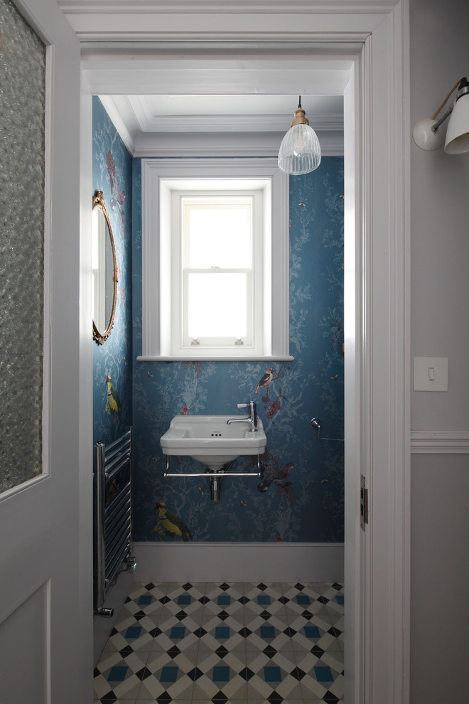 Inredning av ett modernt litet toalett, med en toalettstol med separat cisternkåpa, blå väggar, klinkergolv i keramik, ett väggmonterat handfat och flerfärgat golv