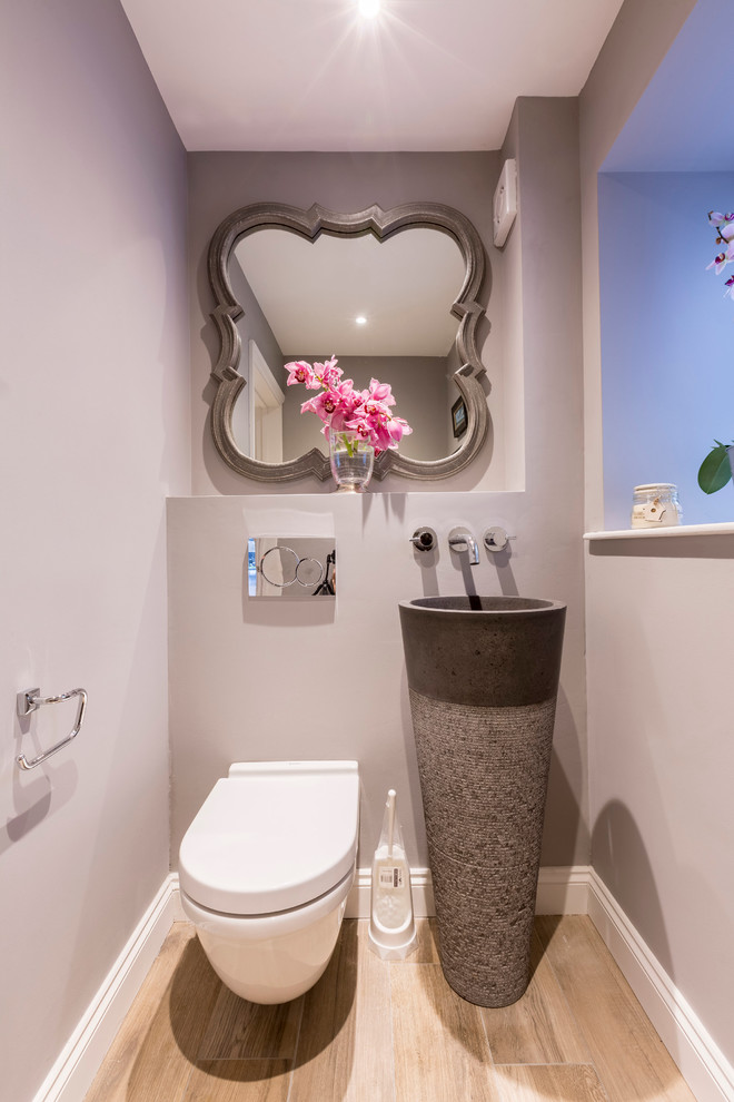 Example of a transitional light wood floor powder room design in London with a wall-mount toilet, gray walls and an integrated sink