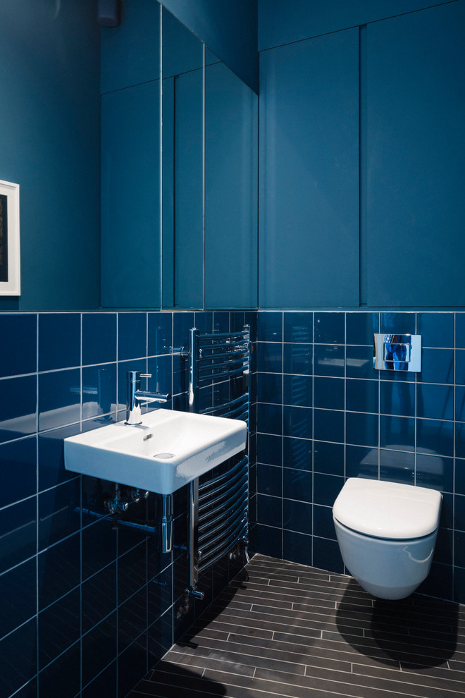 Modelo de aseo actual con sanitario de pared, baldosas y/o azulejos azules, baldosas y/o azulejos de porcelana, paredes azules, suelo de baldosas de porcelana, lavabo suspendido y suelo negro