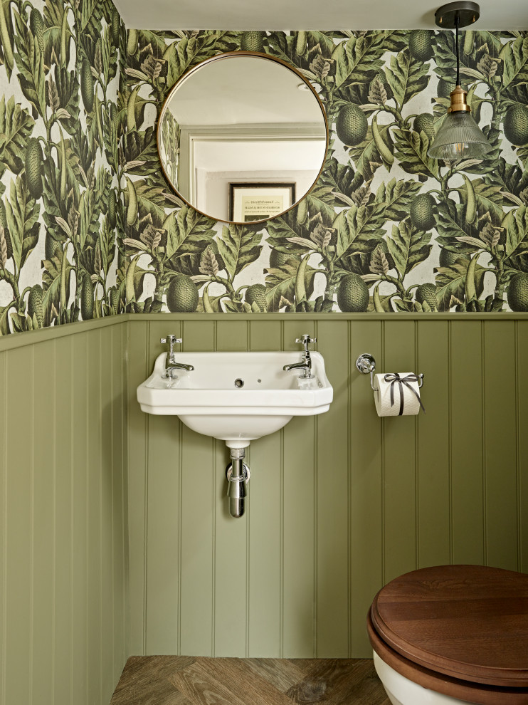 Bild på ett vintage toalett, med gröna väggar, mörkt trägolv, ett väggmonterat handfat och brunt golv