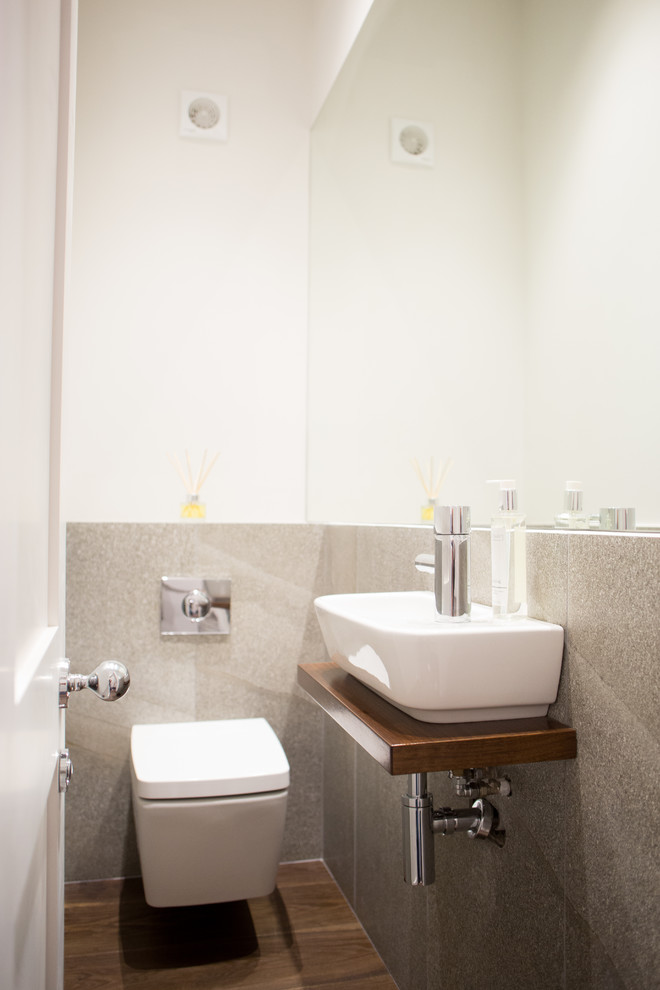 Immagine di un piccolo bagno di servizio minimal con WC sospeso, piastrelle grigie, lastra di pietra, pareti bianche, parquet scuro, lavabo sospeso e pavimento marrone