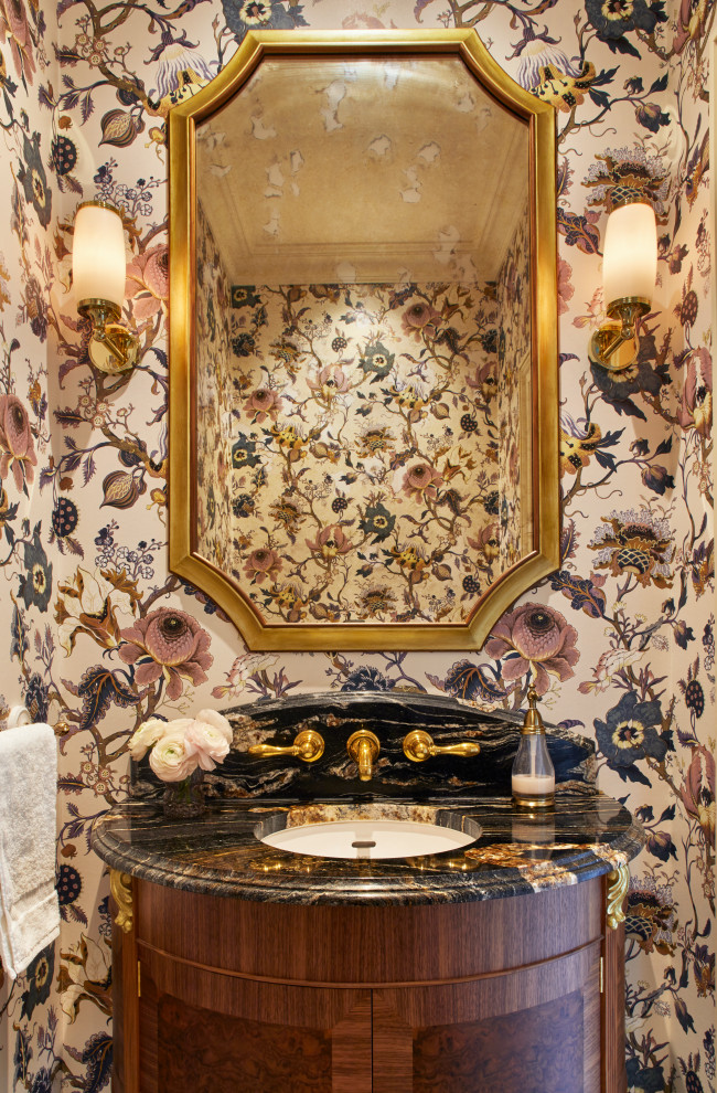 Example of a mid-sized classic ceramic tile, blue floor and wallpaper powder room design in Surrey with brown cabinets, a one-piece toilet, marble countertops, black countertops and a freestanding vanity