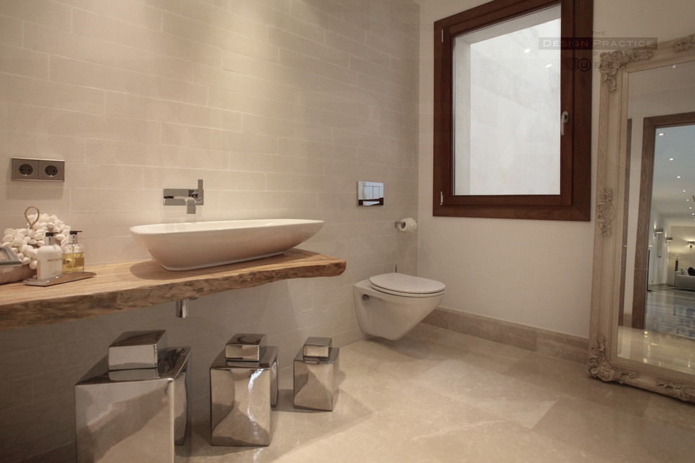 This is an example of a medium sized mediterranean cloakroom in Cheshire with a wall mounted toilet, beige walls, marble flooring and a vessel sink.