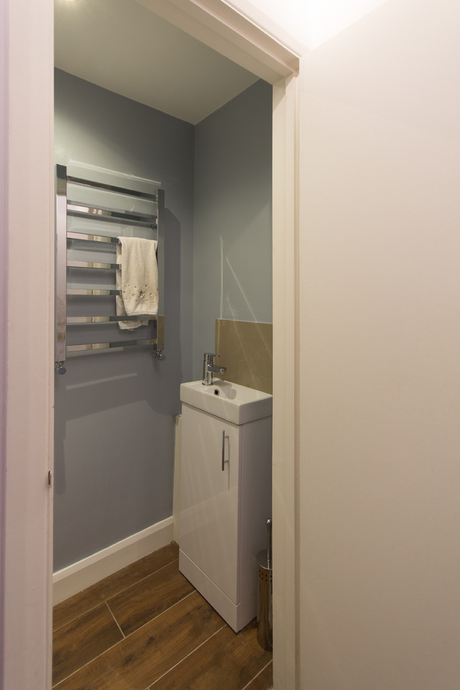 Design ideas for a small modern cloakroom in London with flat-panel cabinets, white cabinets, a one-piece toilet, brown tiles, ceramic tiles, blue walls, porcelain flooring and a built-in sink.