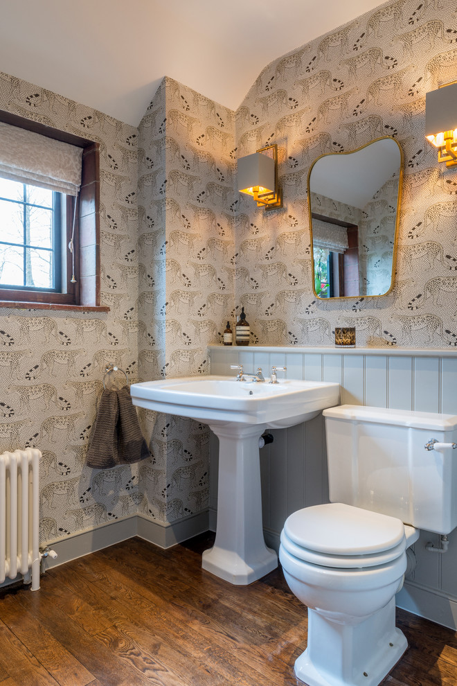 Photo of a farmhouse cloakroom in Surrey with a pedestal sink, a two-piece toilet, grey walls, medium hardwood flooring and brown floors.
