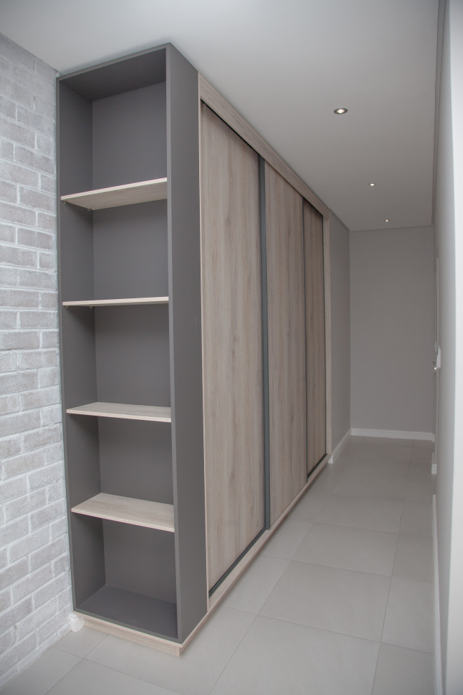 Ejemplo de armario vestidor unisex moderno de tamaño medio con armarios con paneles lisos, puertas de armario de madera clara, suelo de baldosas de porcelana y suelo gris