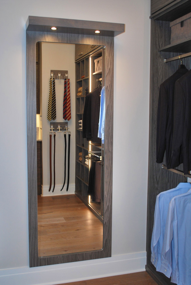 Imagen de armario vestidor de hombre minimalista de tamaño medio con armarios con paneles lisos, puertas de armario grises, suelo de madera en tonos medios y suelo marrón