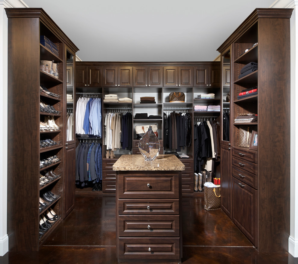 Classic gender neutral walk-in wardrobe in St Louis with raised-panel cabinets, dark wood cabinets, concrete flooring and brown floors.