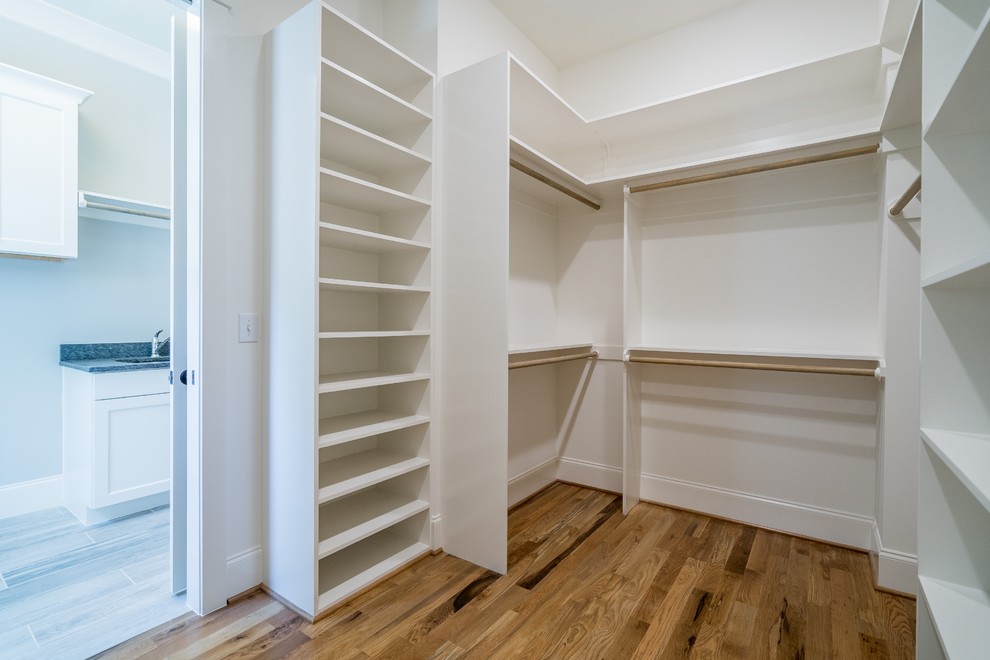 Example of a mid-sized farmhouse medium tone wood floor and brown floor walk-in closet design in Raleigh with white cabinets