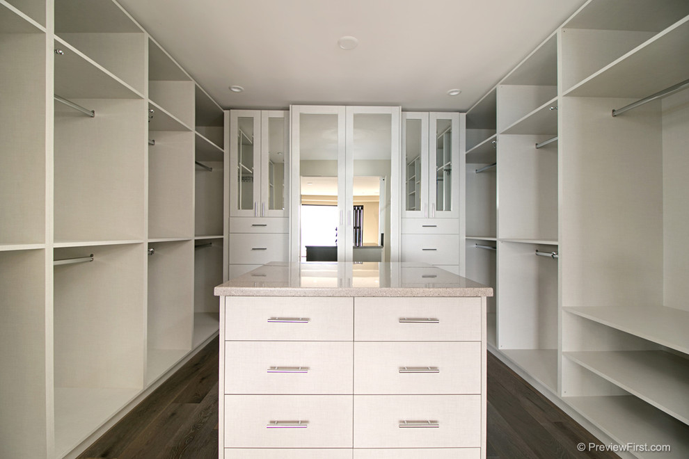 Imagen de armario vestidor unisex costero grande con armarios abiertos, puertas de armario blancas y suelo de madera oscura