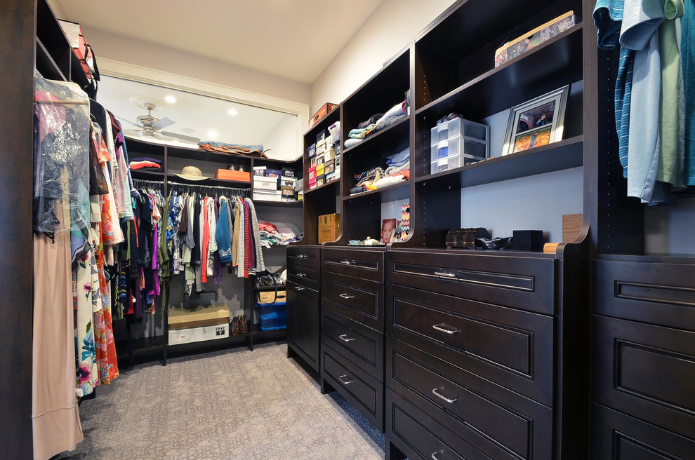 This is an example of a large traditional gender neutral walk-in wardrobe in Austin with raised-panel cabinets, dark wood cabinets and carpet.