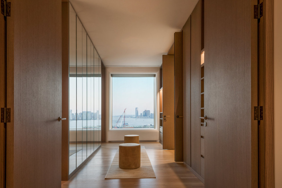 This is an example of a modern walk-in wardrobe in New York with flat-panel cabinets, light wood cabinets, light hardwood flooring and beige floors.