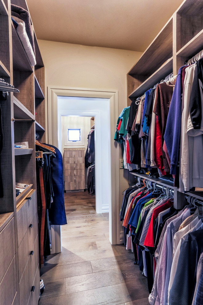Example of a mid-sized country men's medium tone wood floor walk-in closet design in Calgary with flat-panel cabinets and gray cabinets