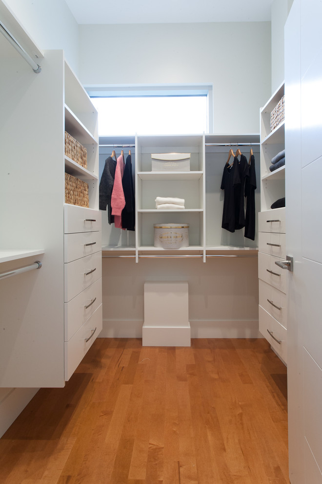 Ejemplo de armario vestidor unisex minimalista con armarios con paneles lisos, puertas de armario blancas y suelo de madera en tonos medios