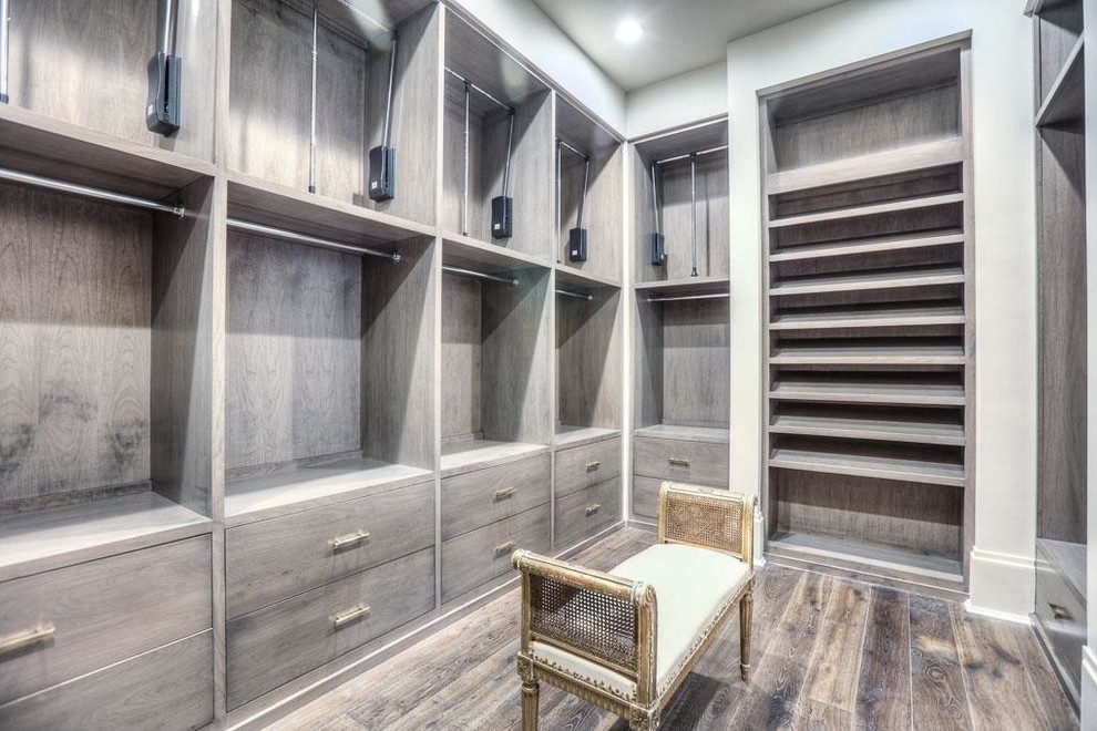 Aménagement d'un grand dressing room classique neutre avec un placard à porte plane, un sol en bois brun et des portes de placard grises.