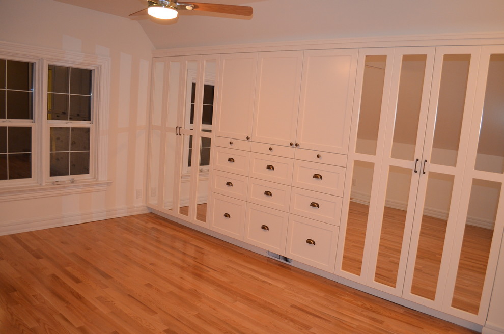 Klassisches Ankleidezimmer mit Schrankfronten im Shaker-Stil, weißen Schränken und hellem Holzboden in Sonstige