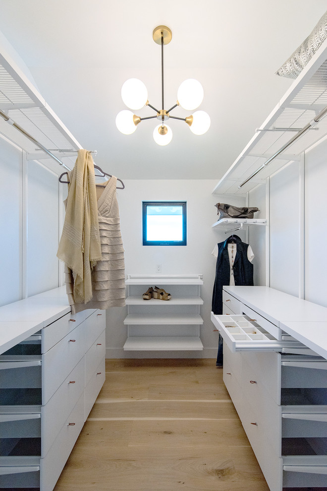 Photo of a large traditional walk-in wardrobe for women in Denver with white cabinets and light hardwood flooring.