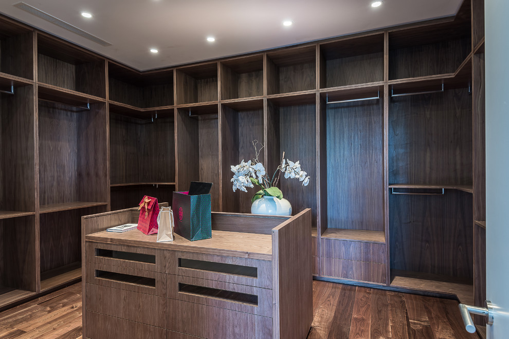 Immagine di una cabina armadio unisex minimalista di medie dimensioni con nessun'anta, ante in legno bruno e parquet scuro