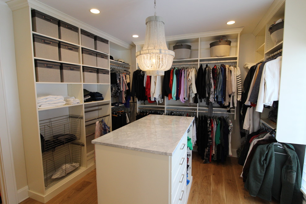 This is an example of a large classic walk-in wardrobe for women in Indianapolis with raised-panel cabinets, beige cabinets, light hardwood flooring and brown floors.