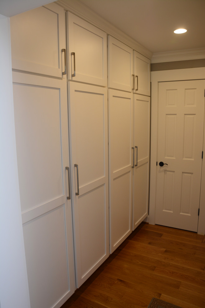 Cette image montre un dressing traditionnel de taille moyenne et neutre avec un placard à porte shaker, des portes de placard blanches, un sol en bois brun et un sol marron.