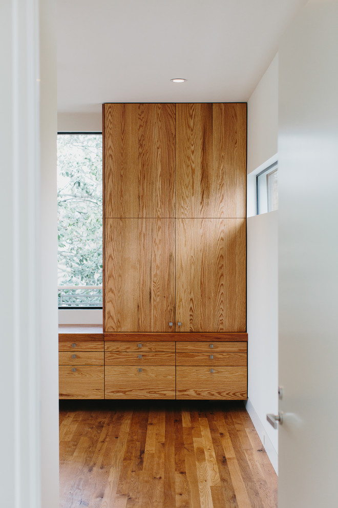 Modelo de armario vestidor unisex moderno de tamaño medio con armarios con paneles lisos, puertas de armario de madera oscura y suelo de madera en tonos medios