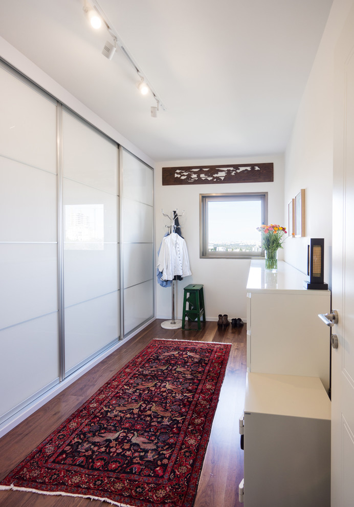 Imagen de armario vestidor unisex contemporáneo de tamaño medio con armarios tipo vitrina, puertas de armario blancas y suelo de madera oscura