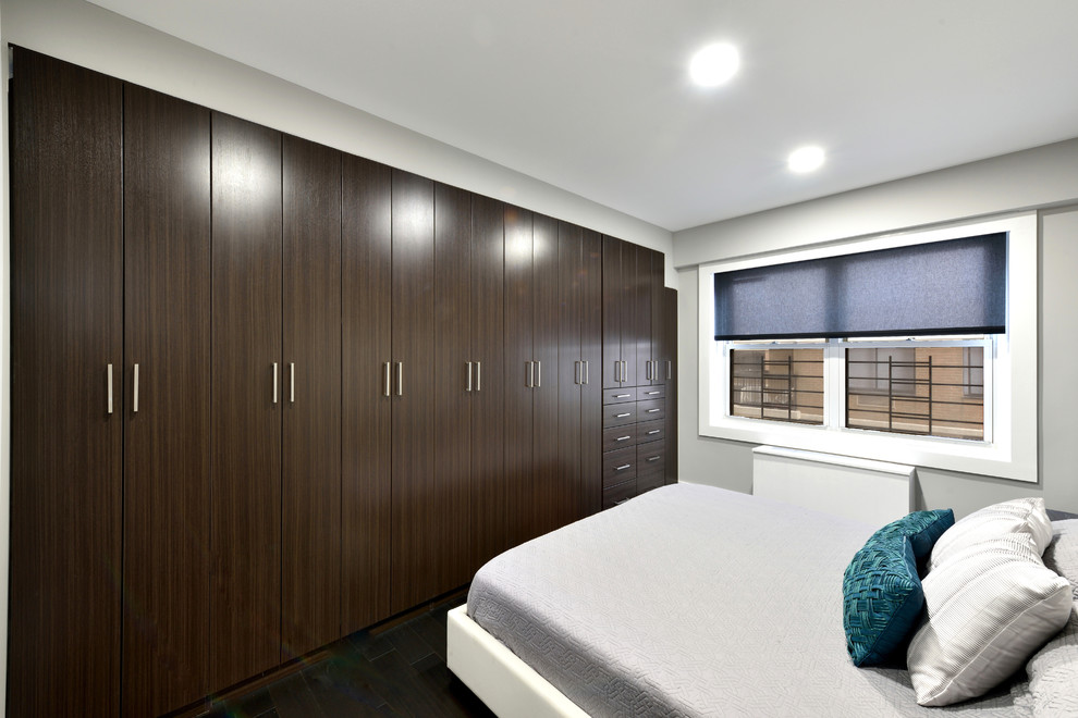 Diseño de armario unisex actual pequeño con armarios con paneles lisos, puertas de armario de madera en tonos medios y suelo de madera oscura