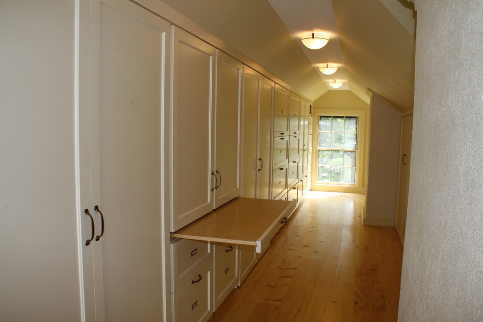 Inredning av ett klassiskt litet walk-in-closet för könsneutrala, med vita skåp och ljust trägolv