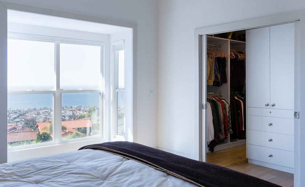 Diseño de armario vestidor unisex contemporáneo pequeño con armarios con paneles lisos, puertas de armario blancas y suelo de madera clara