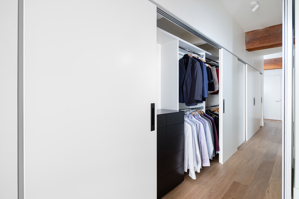 Inspiration for a mid-sized modern gender-neutral light wood floor and brown floor reach-in closet remodel in Vancouver with flat-panel cabinets and white cabinets