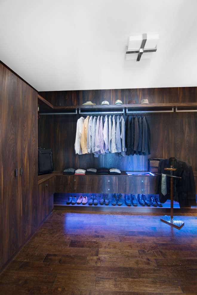 Ejemplo de armario vestidor de hombre contemporáneo grande con armarios con paneles lisos, puertas de armario de madera en tonos medios y suelo de madera oscura