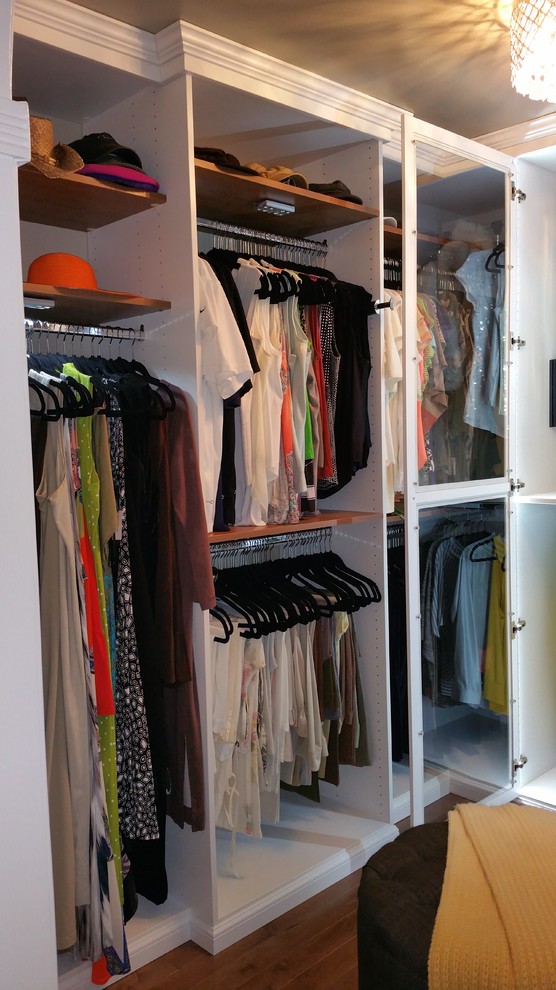Diseño de armario vestidor de mujer clásico renovado de tamaño medio con armarios tipo vitrina, puertas de armario blancas y suelo de madera en tonos medios
