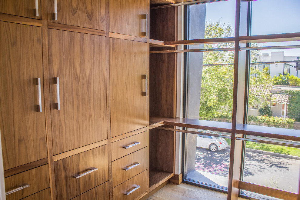 Imagen de armario vestidor unisex actual de tamaño medio con armarios con paneles lisos, puertas de armario de madera oscura, suelo de madera clara y suelo marrón