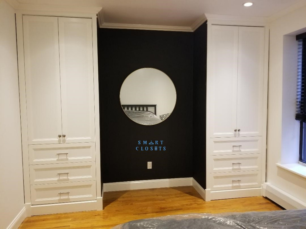 Kleines, Neutrales Shabby-Chic Ankleidezimmer mit Ankleidebereich, profilierten Schrankfronten, weißen Schränken, braunem Holzboden und braunem Boden in New York