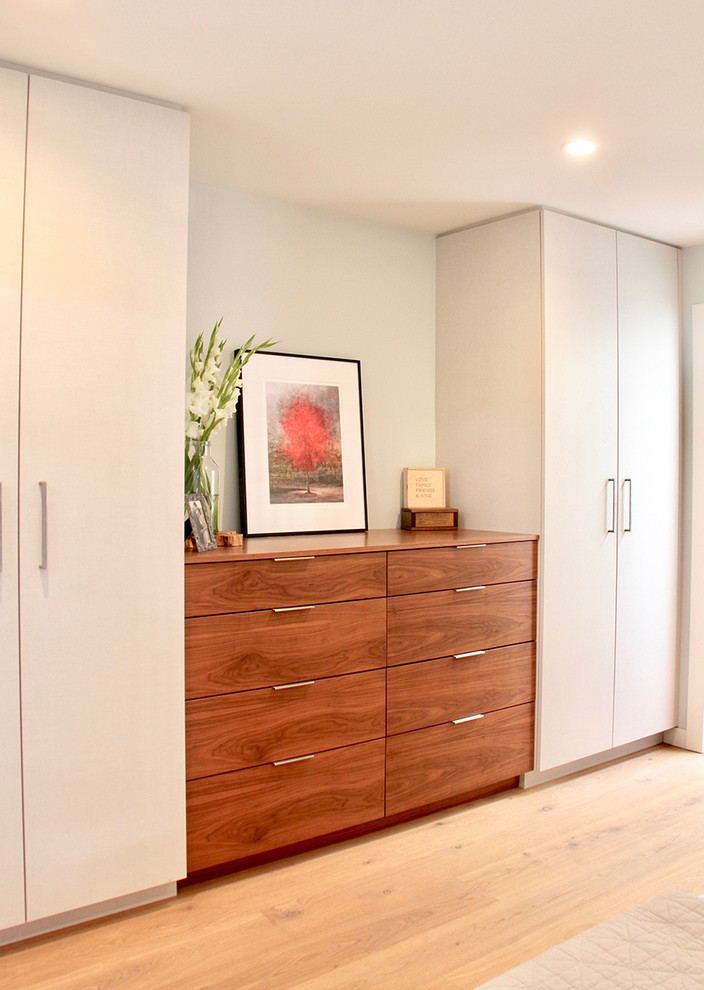 Photo of a small modern gender neutral standard wardrobe with flat-panel cabinets, medium wood cabinets, light hardwood flooring and brown floors.