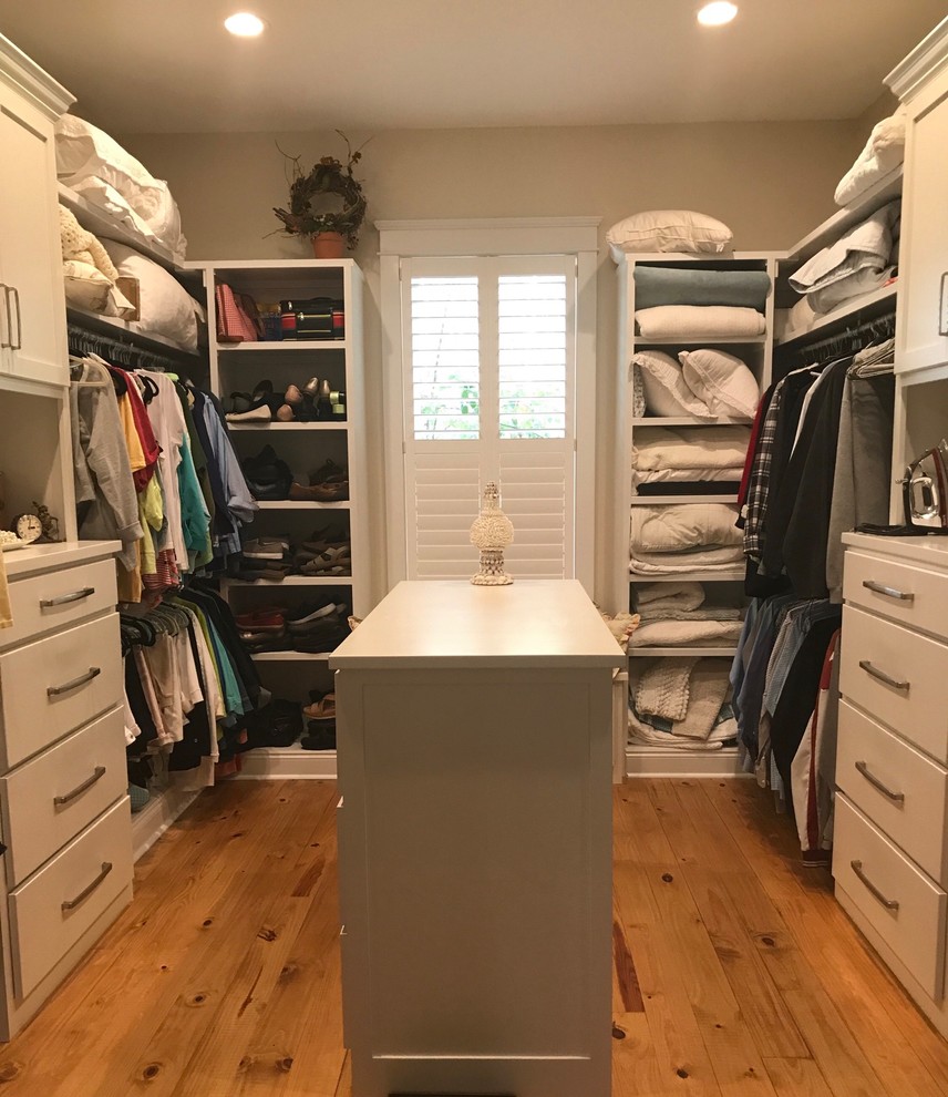 Diseño de armario vestidor unisex clásico de tamaño medio con puertas de armario blancas, suelo de madera en tonos medios y suelo marrón