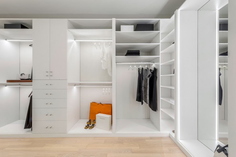 Photo of a large contemporary walk-in wardrobe for women in New York with flat-panel cabinets, white cabinets, light hardwood flooring and beige floors.